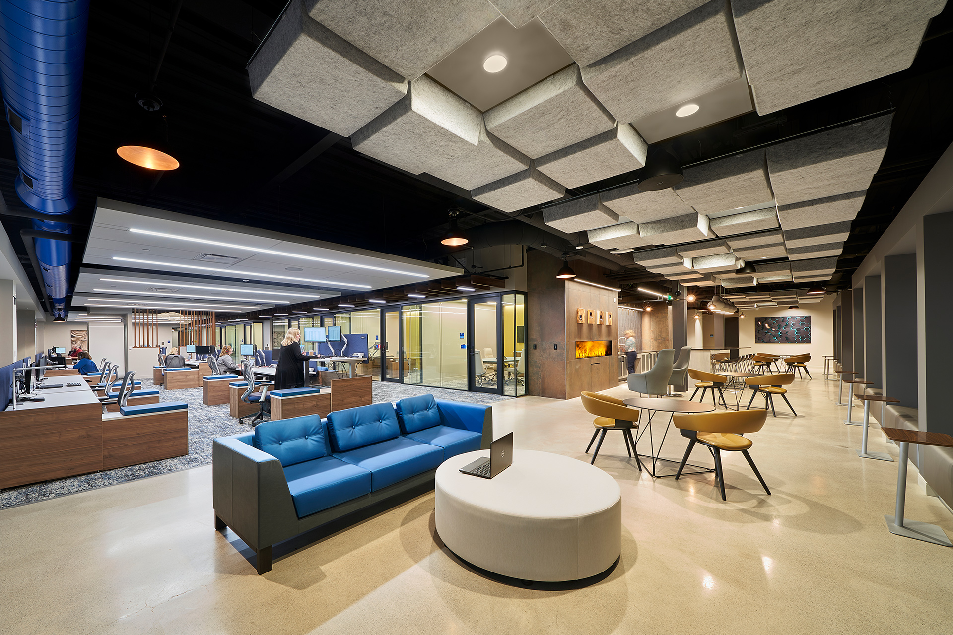 One of the lounges at Blue Foundry Bank, including a coffee station and a variety of different seating options. The adjacent open work area, which some staff working at standing desks, is also shown.