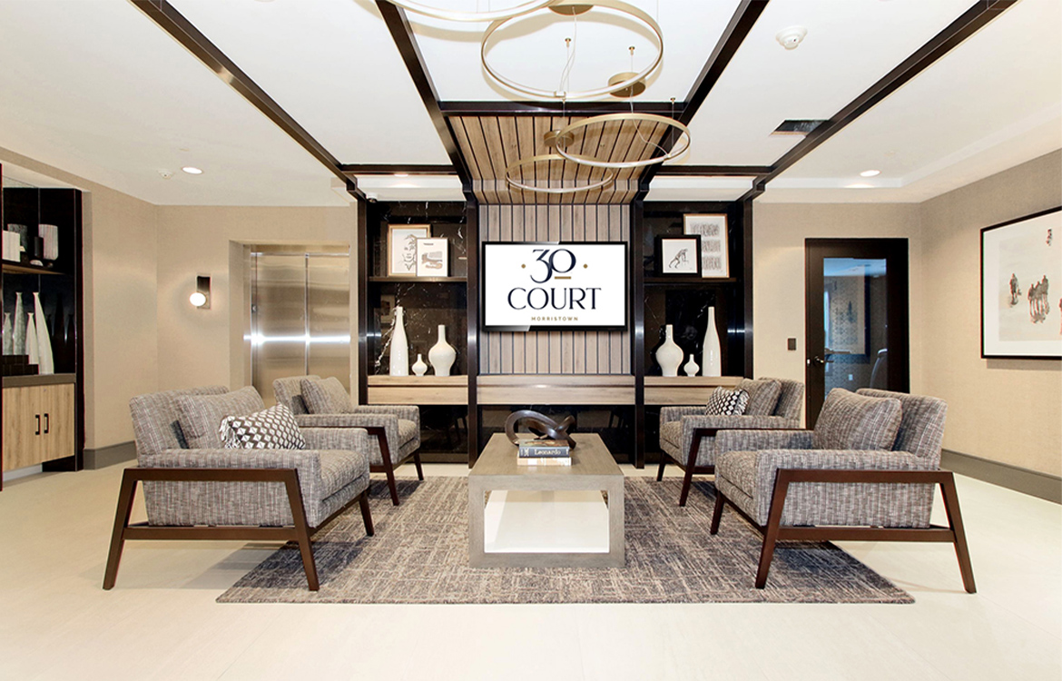 The main lobby at the 30 Court Street residential development is covered in detail and warm colors, from a coffered ceiling to an abundance of metal, wood tones and dimension through panels installed on the wall.