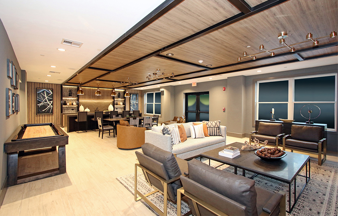 The resident lounge at the 30 Court Street residential development is covered in detail and warm colors, from a coffered ceiling to an abundance of metal and wood tones. There are sofa, chairs and large dining table, a bar and a shuffleboard table.