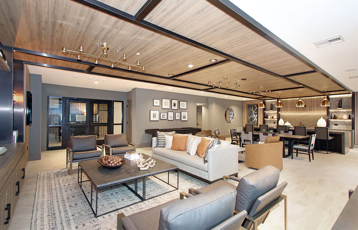 The resident lounge at the 30 Court Street residential development is covered in detail and warm colors, from a coffered ceiling to an abundance of metal and wood tones. There are sofa, chairs and large dining table and a bar.