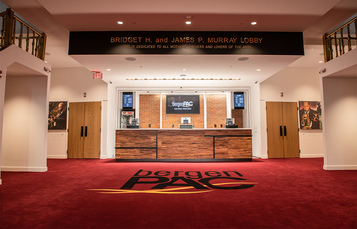The new lobby area of bergenPAC, showing a bar and point-of-sale system in a space that includes eclectic light installations and exposed brick.