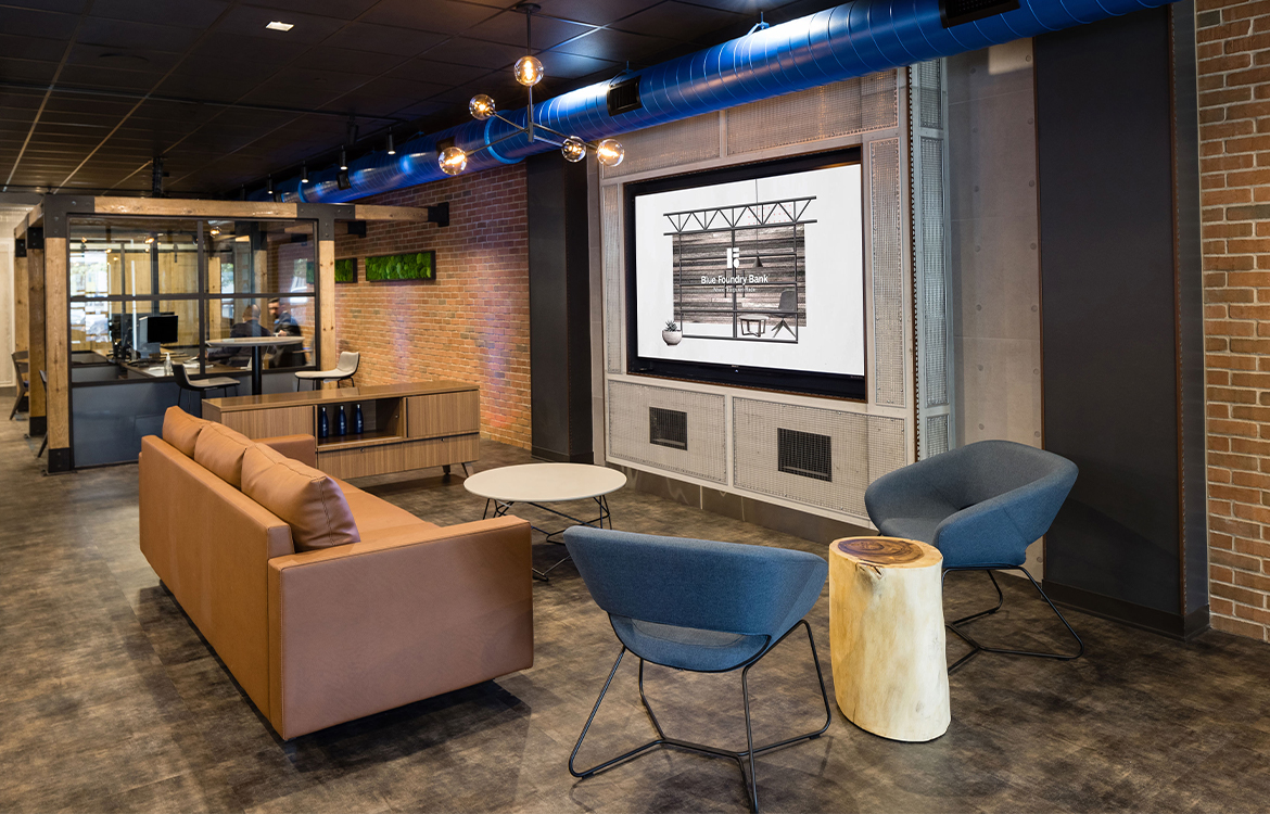 The Blue Foundry Bank branch in Ridgewood, NJ, arranged like a living room, with a sofa, chairs and a large screen, a signature feature of Blue Foundry Bank branch designs.