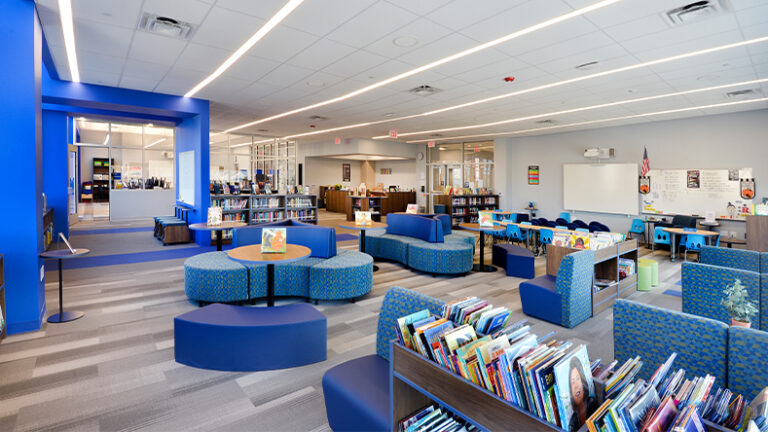 The media center at the Blanquita B. Valenti Community School, showing flexible furniture, book storage and in the distance, the glass-enclosed makerspace.