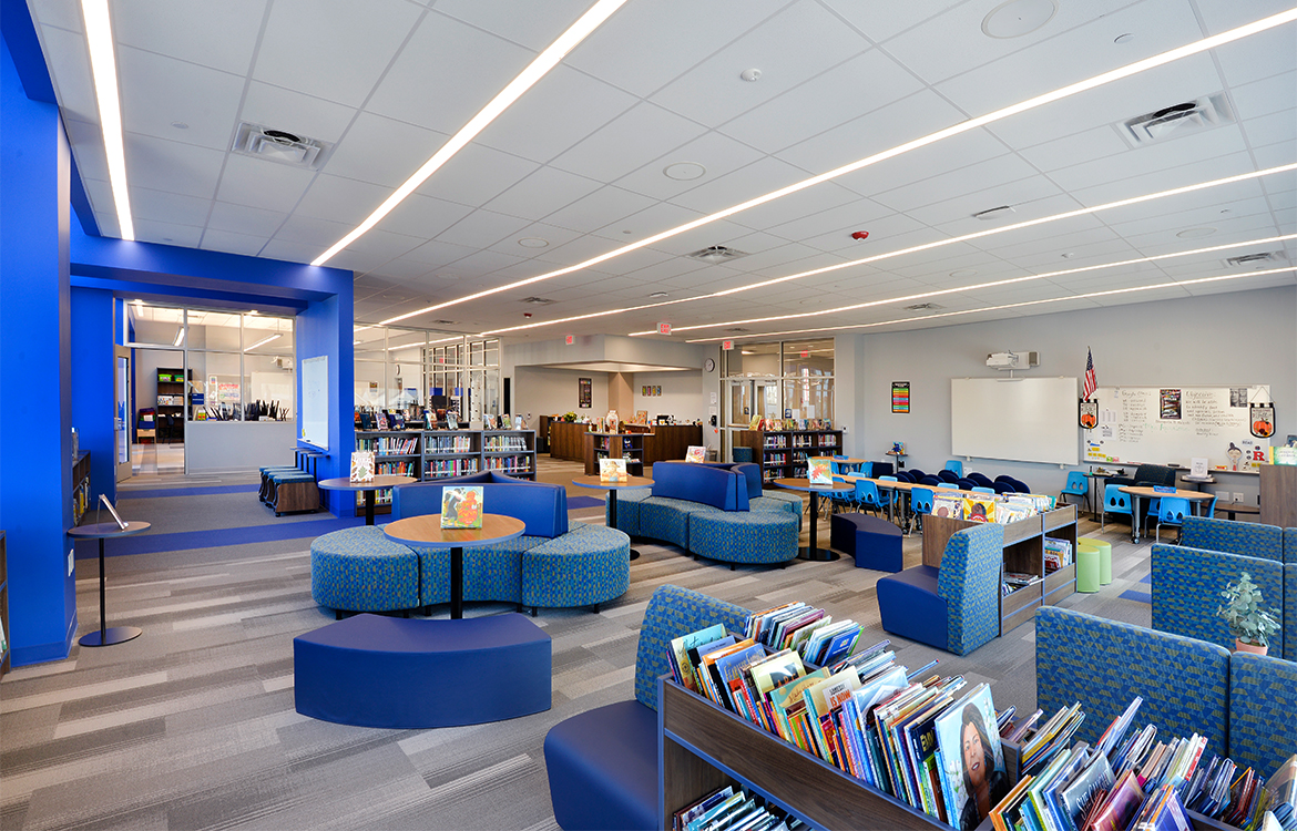 The media center at the Blanquita B. Valenti Community School, showing flexible furniture, book storage and in the distance, the glass-enclosed makerspace.