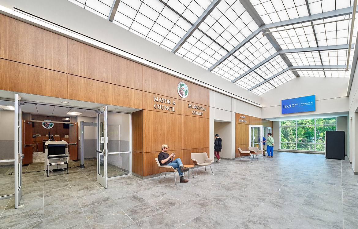 The lobby of the Ridgefield Municipal Complex, which overlooks the court entrance and court payments office. The space is flooded with natural light thanks to a skylight the runs the entire length of the building and in the distance, large windows connect the building to nearby nature.