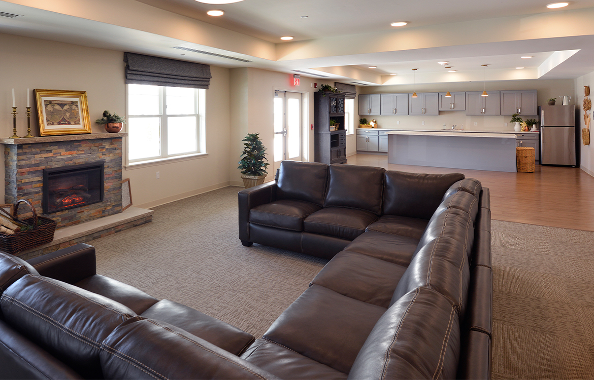 An oversized sofa in a large gathering area for residents at The Residences at Upper Saddle River, overlooking the kitchen with an island for gathering.