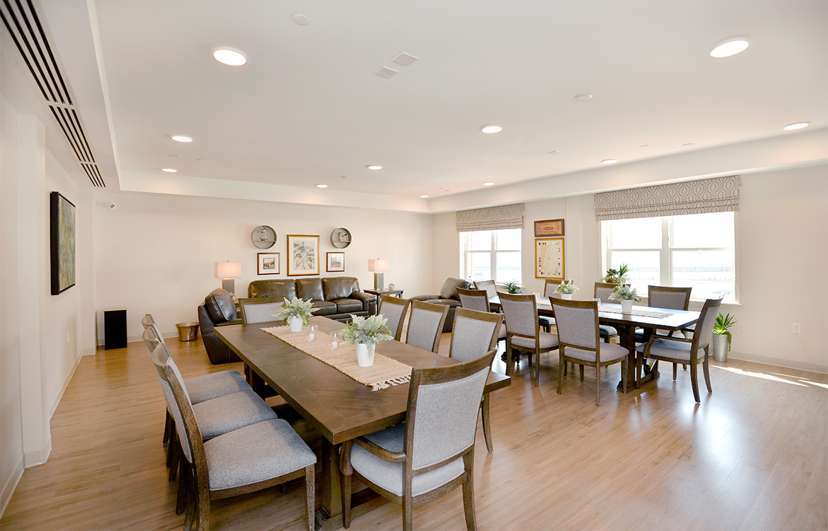 A community dining room at The Residences at Upper Saddle River, showing two tables with seating for eight each, as well as a sofa and chairs.